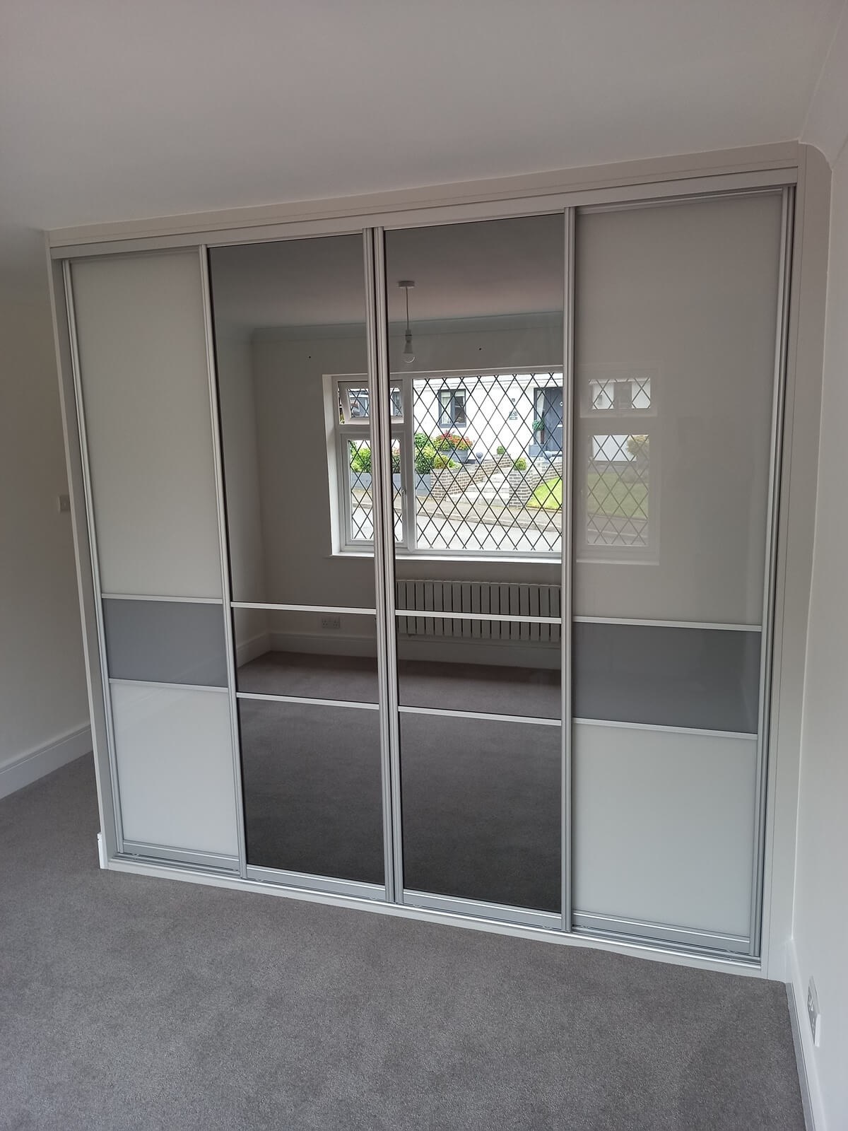 Fitted sliding wardrobe in Aldridge with a white frame, grey glass and full-panel silver mirror doors