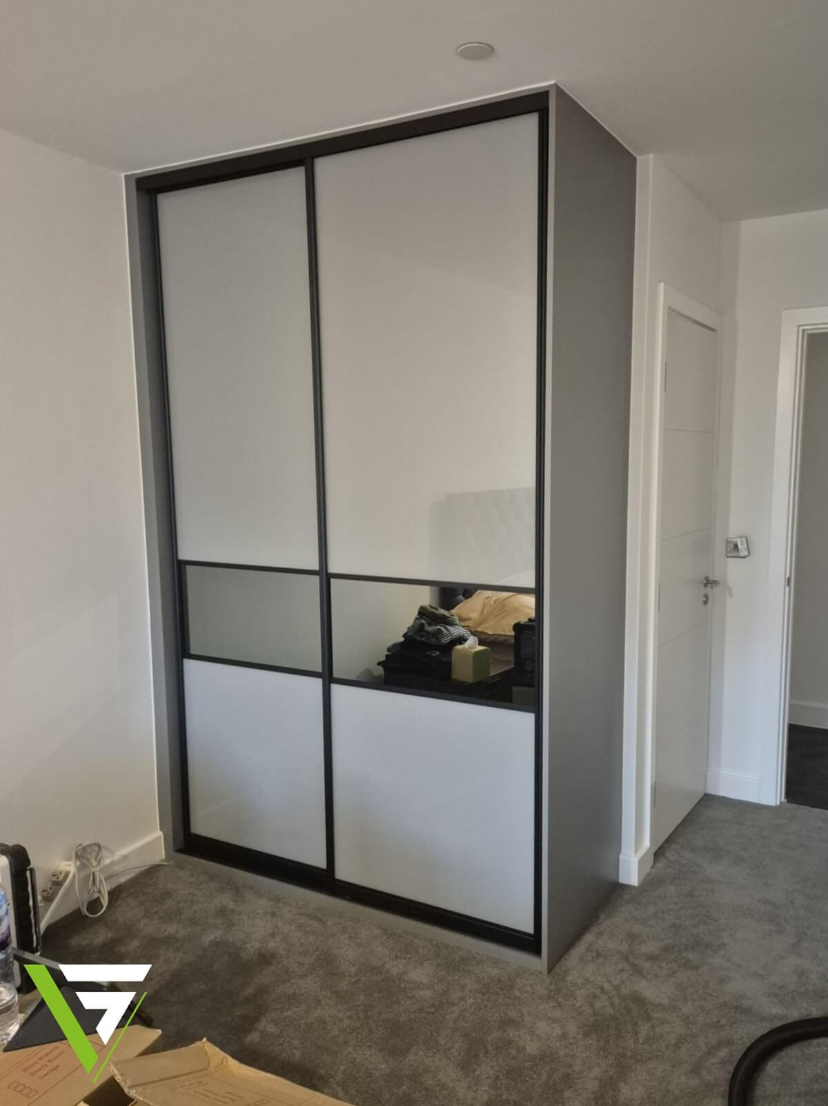 Grey and black-framed sliding wardrobe with frosted glass and mirror panels, built around the corner of a bedroom