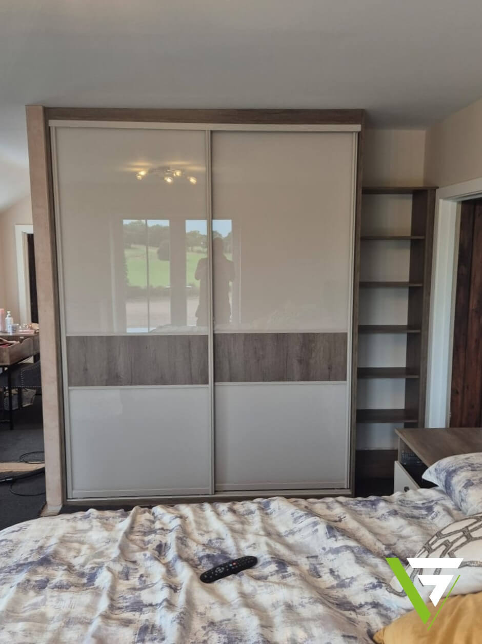 Mushroom-framed sliding wardrobe with an oak-effect band, paired with open shelving in a sloped-ceiling bedroom