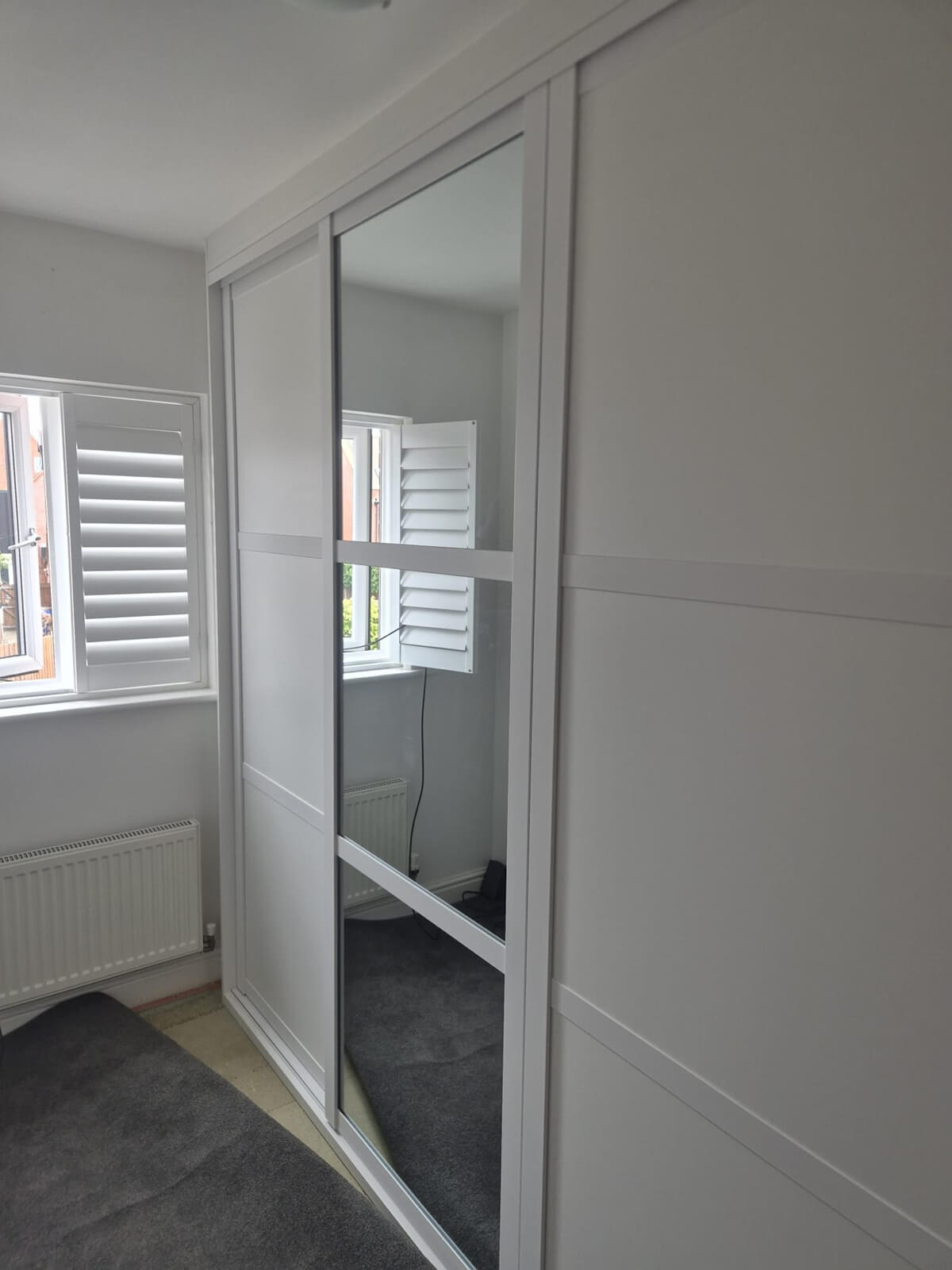 White-framed sliding wardrobe with a mirror door and plain panels, fitted floor-to-ceiling across a bedroom wall