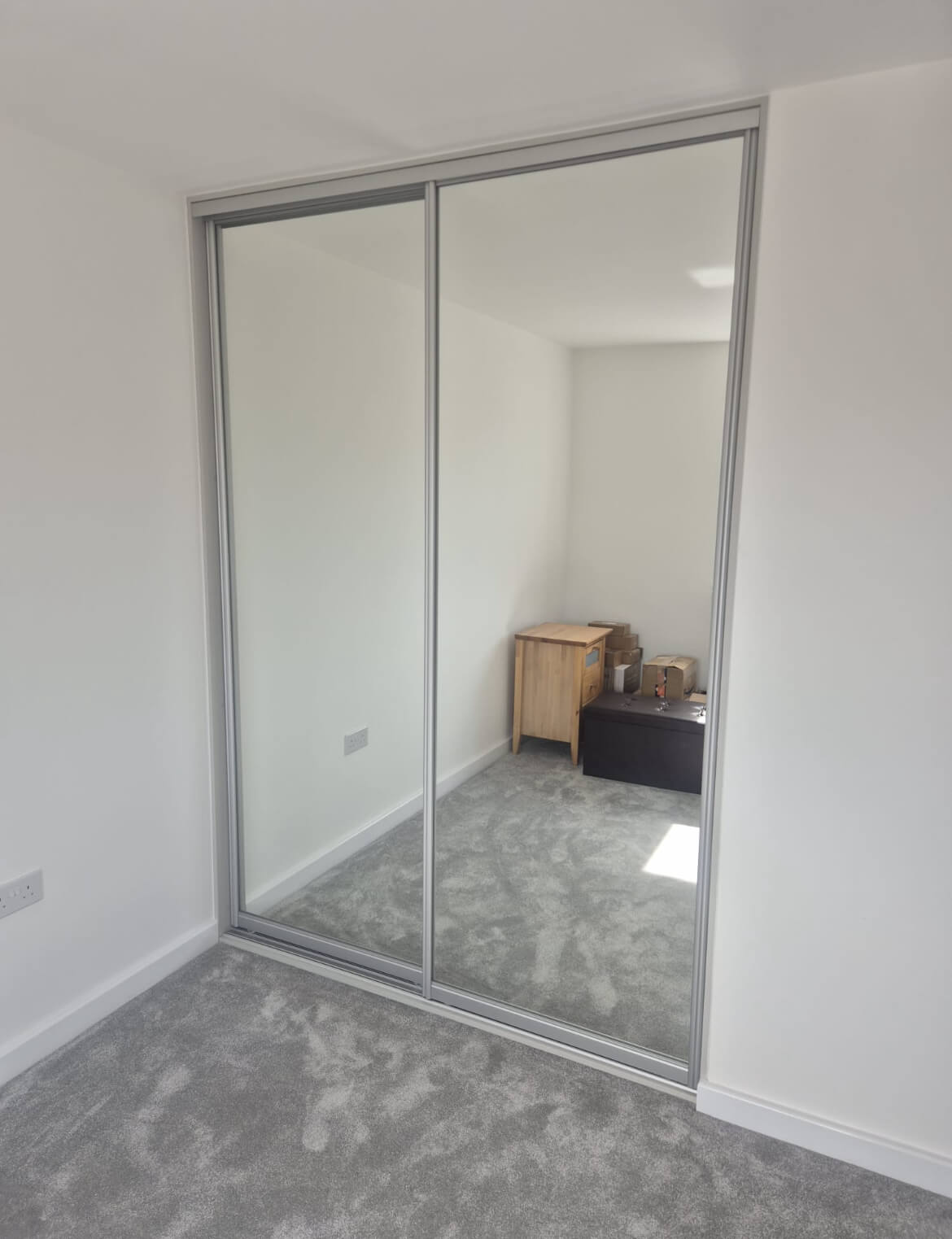 Two full-height silver mirror sliding doors on a silver FORM frame, fitted into a recess in a Stafford bedroom