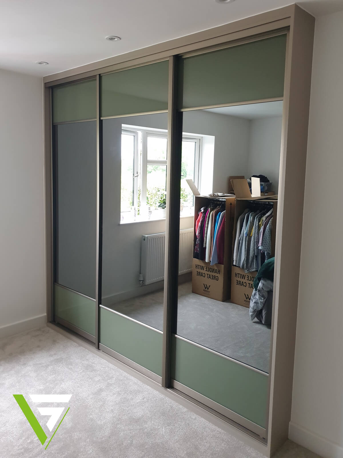Three VERTEX split-panel sliding wardrobe doors in green glass and mirror, filling a bedroom wall in Stafford