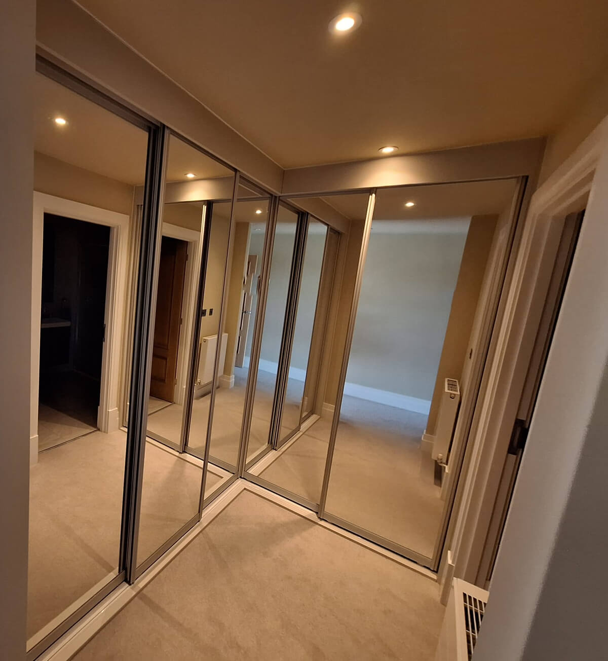 L-shaped run of silver mirror sliding wardrobe doors on a FORM frame in a dressing area in Tamworth