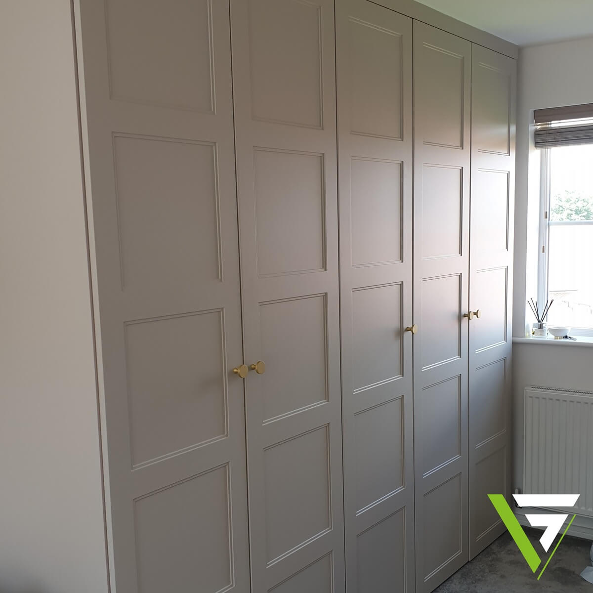 Cashmere four-panel hinged fitted wardrobes in a Birmingham bedroom with brass bar and knob handles