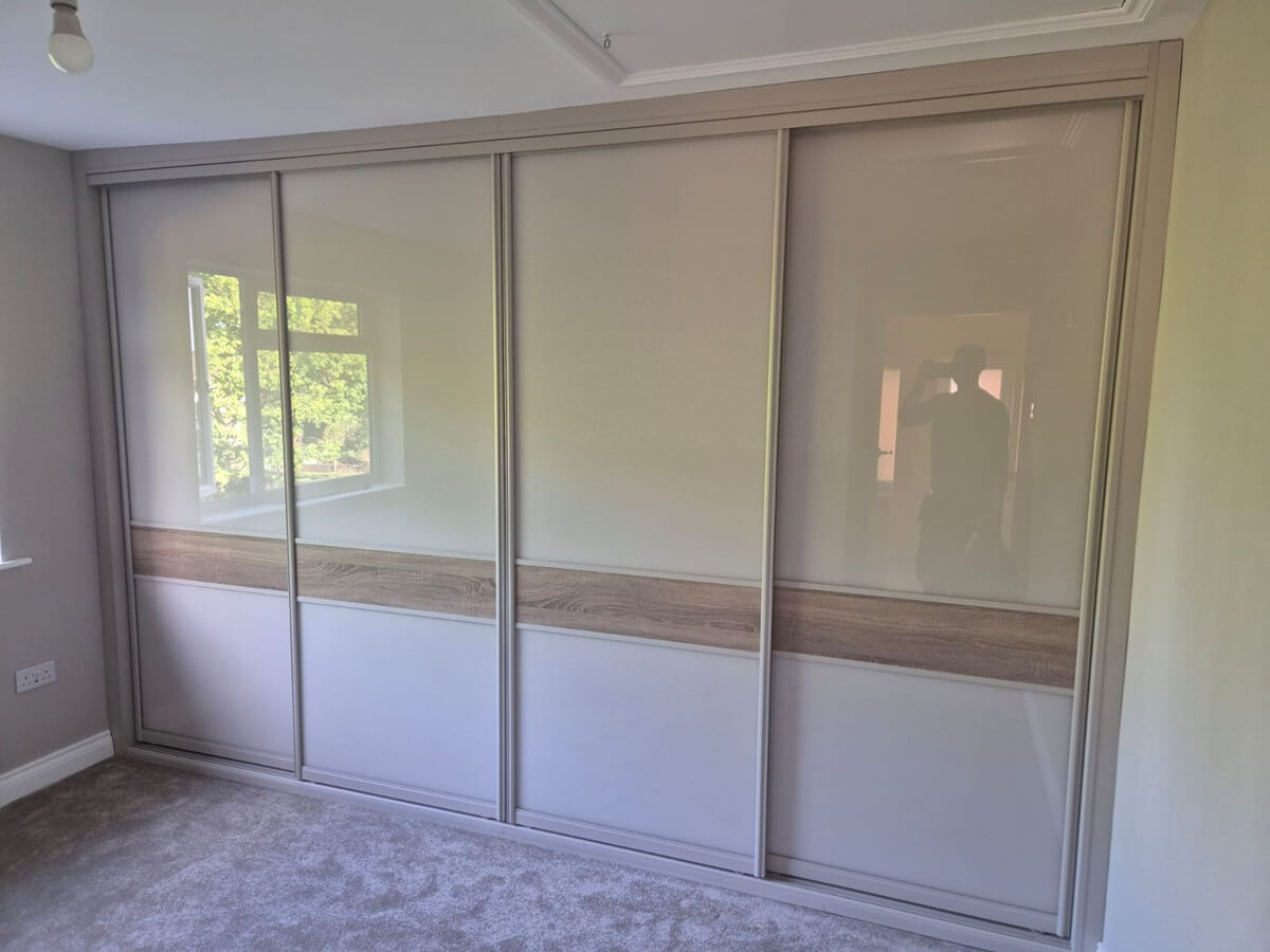 Four-door sliding wardrobe with a cashmere FORM frame, cream glass panels and a grey Bardolino oak split band, fitted in a loft bedroom