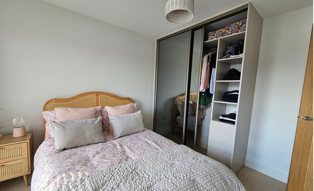 Two-door grey-glass sliding wardrobe with a cashmere frame, alongside an open shelf tower and drawers holding folded clothes