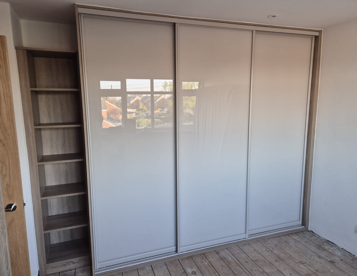 Three-door sliding wardrobe with an oak-effect Bardolino frame and cream glass doors, next to a matching open shelf tower