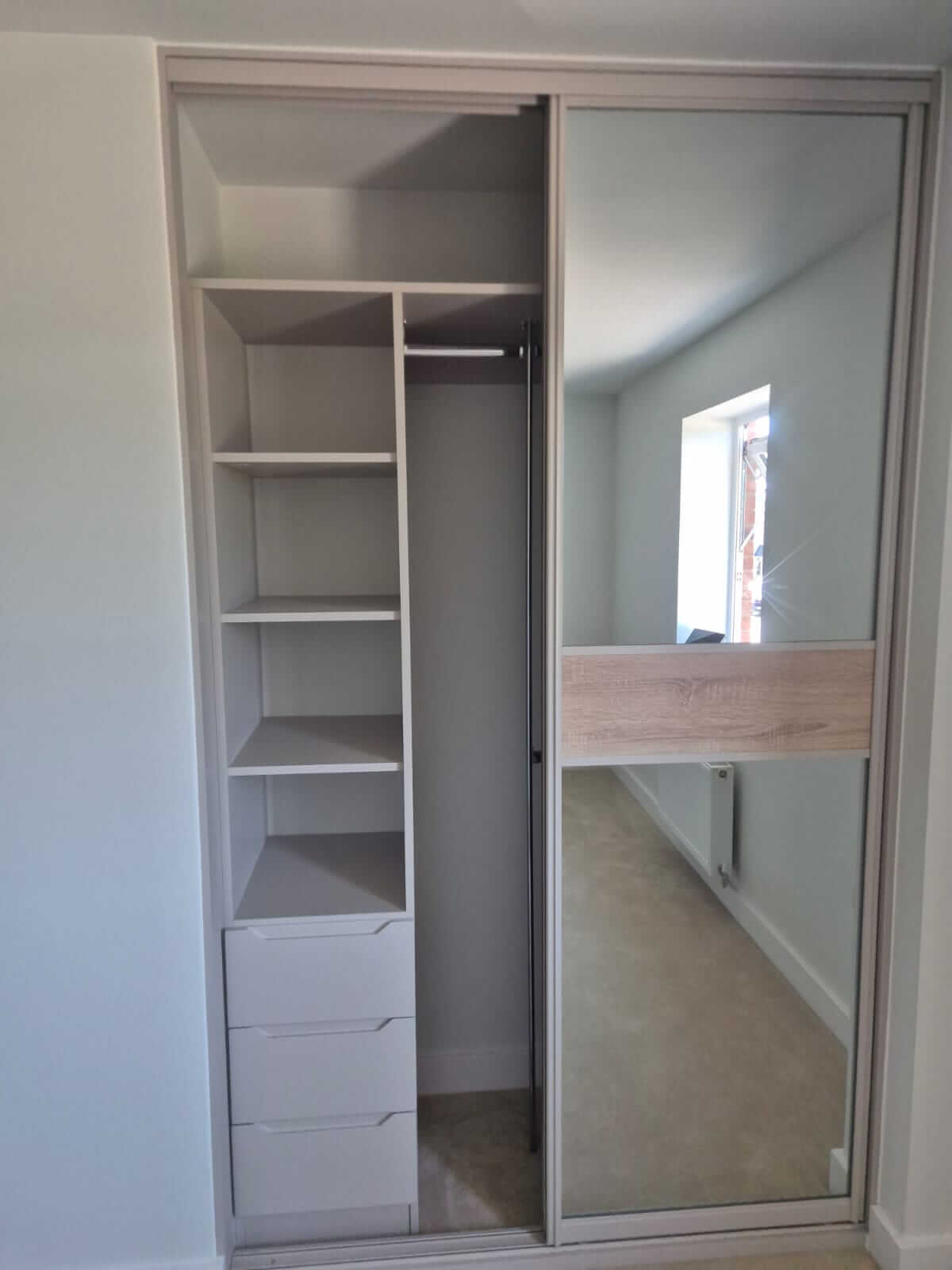Open sliding wardrobe — shelves, three drawers and a hanging rail behind a silver mirror door with a Grey Nebraska Oak split; bespoke wardrobe interiors across Sutton Coldfield