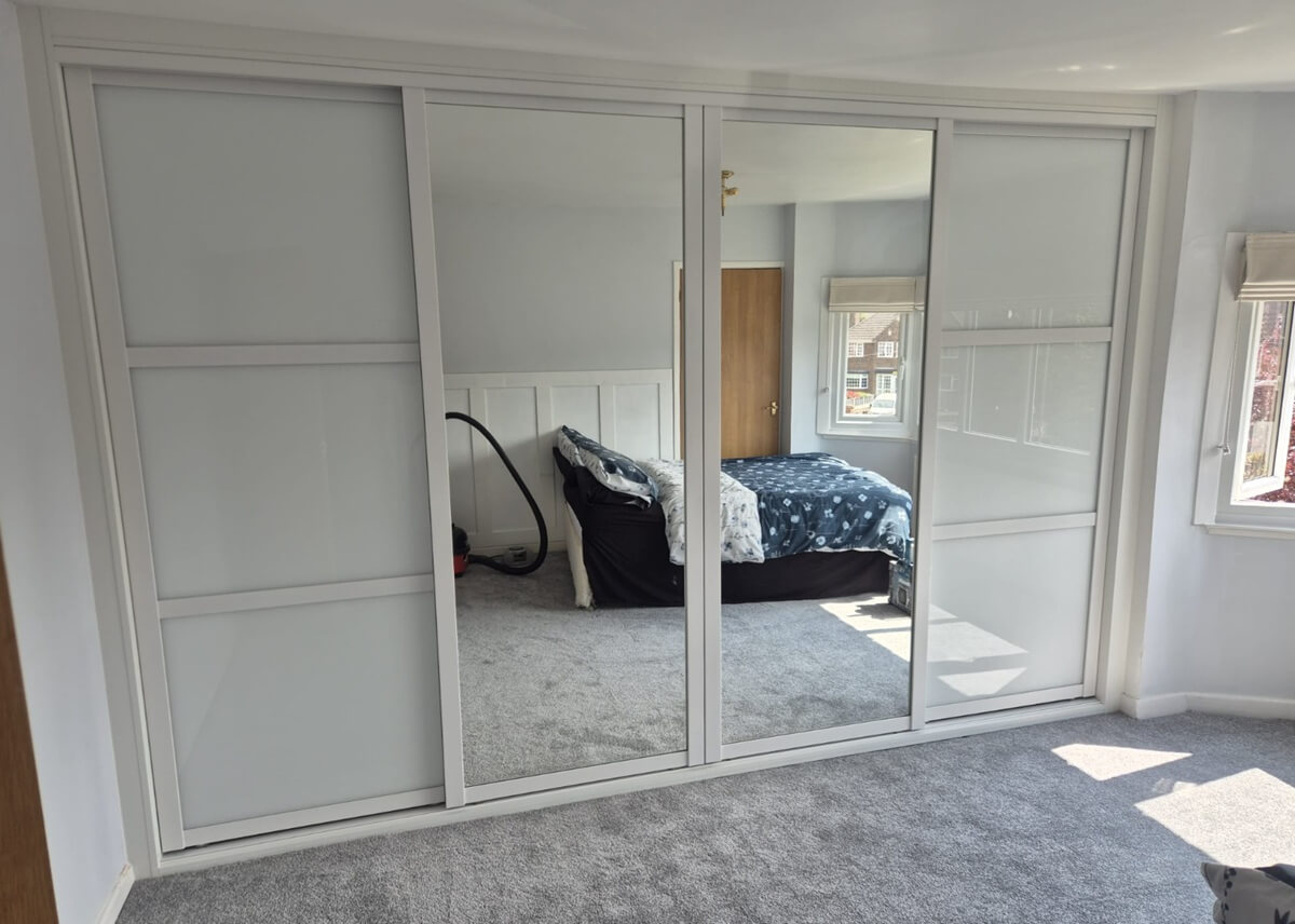 Four-door sliding wardrobe with a white frame, combining white shaker-style glass panels and silver mirror doors