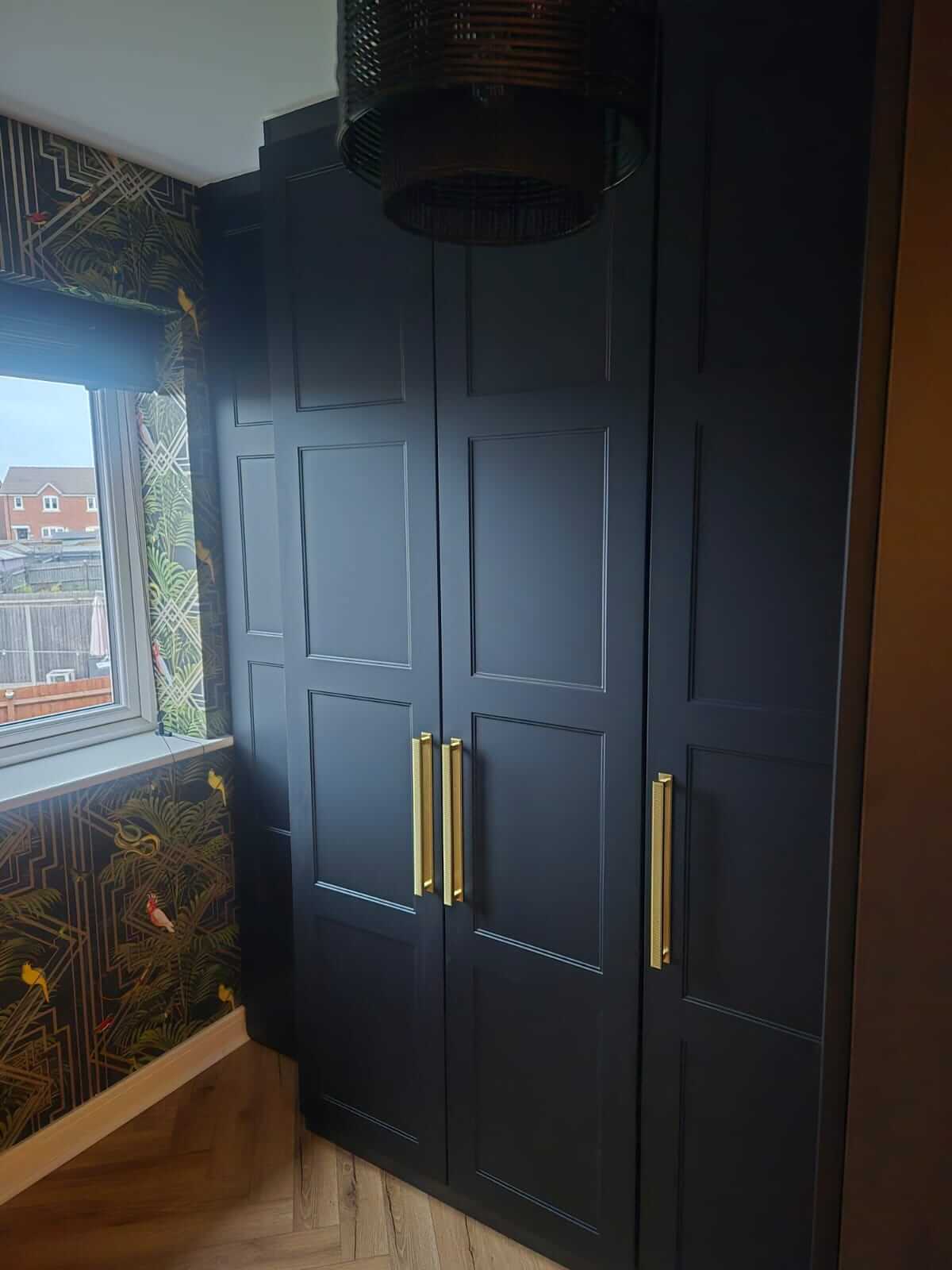Black shaker hinged wardrobe doors with brass bar handles in an L-shaped dressing room in Aldridge
