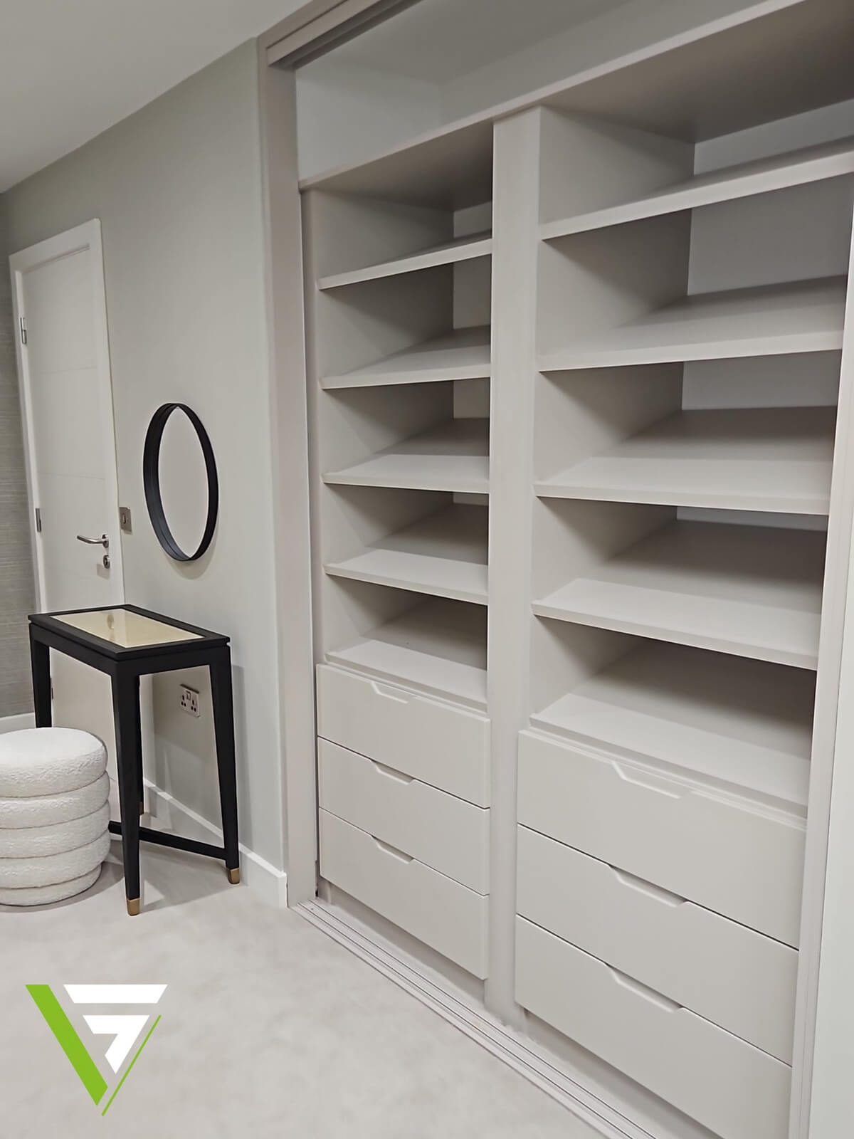 Custom shelf stacks above two banks of handleless drawers, built into a dressing area with a round wall mirror