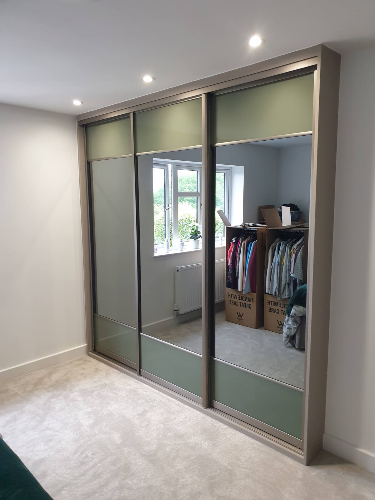 VERTEX split-panel sliding wardrobe doors in green with mirror centre panels in a bedroom in Stafford