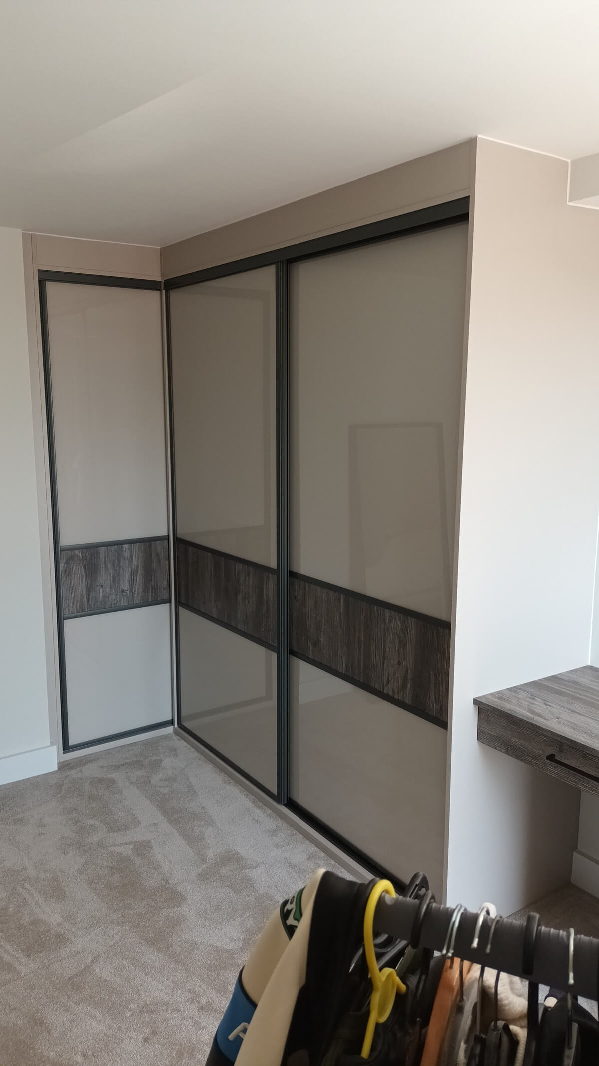 Corner sliding wardrobe with grey glass and a dark oak split, housing a bespoke fitted interior