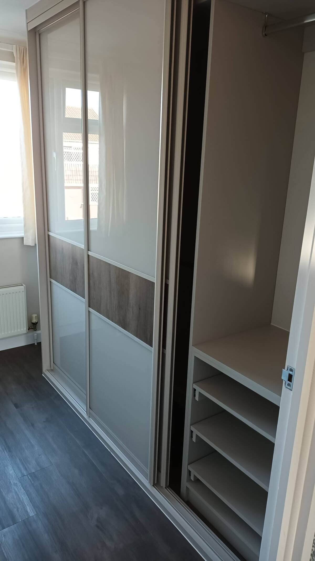 Fitted wardrobe interior with pull-out shoe shelves and a hanging rail behind sliding doors