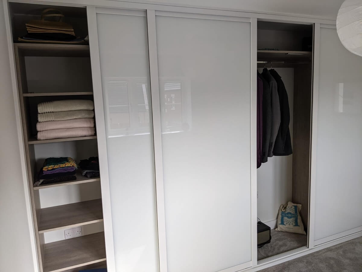 White fitted wardrobe interior with open shelves of folded clothes and towels beside a hanging rail